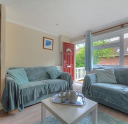 A living room with two blue sofas a white coffee table and a red front door at 36 Fernhill Heights in Charmouth