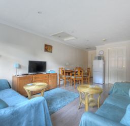 A living room with two blue sofas a wooden TV stand with a television and a dining table with chairs at 36 Fernhill Heights in Charmouth