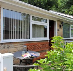 An outdoor seating area with a round table, bench, chair, and greenery at 36 Fernhill Heights Charmouth