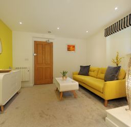 A living room with a yellow sofa a white coffee table a white sideboard and a wooden door at Seashore in Lyme Regis