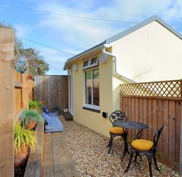 A narrow outdoor patio with wooden fencing a small table with two chairs and cushions and plants along a bench at Seashore in Lyme Regis