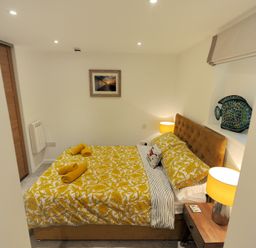 A bedroom with a bed with yellow floral bedding yellow lamps and a wooden nightstand at Seashore in Lyme Regis