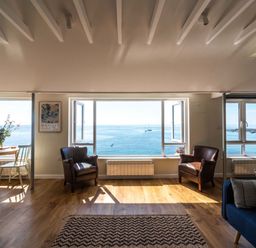 A living room with two leather armchairs a round wooden table with chairs and large windows showing a sea view at 3 Beach Way House Lyme Regis