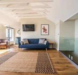 A sitting area with a blue sofa, leather armchair, wall-mounted tv, artwork, and wooden floor at 3 Beach Way House Lyme Regis