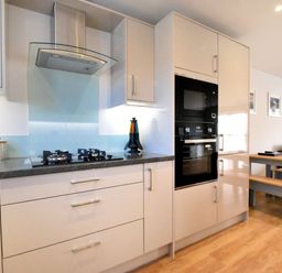 A modern kitchen with a stove gas cooktop hood oven microwave and pantry cabinets next to a dining table and bench seating at Shire View in Lyme Regis