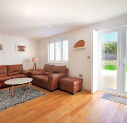 A living room with brown leather sofas a round coffee table a lamp and large glass doors at Shire View in Lyme Regis