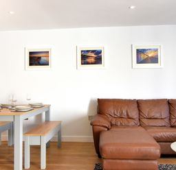 A living area with a brown leather sofa and a dining table with benches and plates on it at Shire View in Lyme Regis