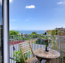 A balcony with a wooden table and chair two wine glasses and a bottle overlooking the sea at Bay View in Lyme Regis