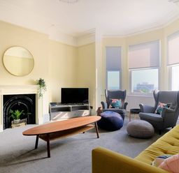 A living room with a yellow sofa two gray armchairs a wooden coffee table a TV on a stand and a fireplace at 7 Seafield Road in Seaton