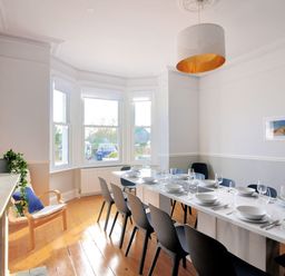 A dining room with a long white table set with dishes and glasses and black chairs around at 7 Seafield Road in Seaton
