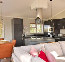 A kitchen and dining area with a wooden table and brown chairs next to a gray sofa with pillows at Hazelwood 4 @ Pinewood Retreat in Pinewood