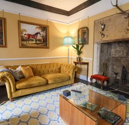 A living room with a yellow sofa paintings of horses on the wall and a stone fireplace at Old Monmouth in Lyme Regis
