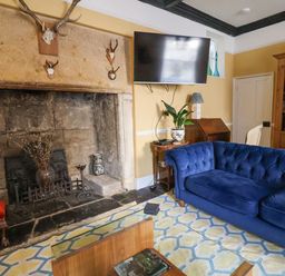 A living room with a blue sofa a stone fireplace mounted television and wooden bookshelf at Old Monmouth in Lyme Regis