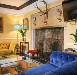 A living room with a blue sofa a yellow sofa a glass coffee table and a fireplace with mounted antlers at Old Monmouth in Lyme Regis