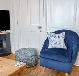 A living room with a blue armchair and a television at The Little Rose in Lyme Regis