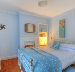 A bedroom with a white metal bed blue polka dot blanket a wooden desk with a TV and a bookshelf with a lamp at Driftwood Lyme Regis