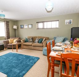 A living room with sofas a blue rug a dining table set with dishes and fruit bowl at Sunny Haven in Preston