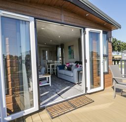 A deck with outdoor chairs and table looking into a living room with sofa and dining table at Away Daze in Carnaby near Bridlington