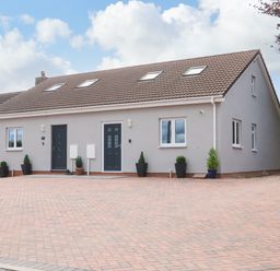 A brick paved driveway in front of a two door gray house with skylights and potted plants at Sawtons Cottage 2 in Dawlish