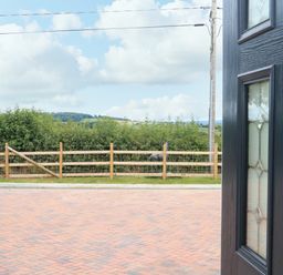 View through an open door showing a paved driveway a wooden fence green bushes and hills in the distance at Sawtons Cottage 2 in Dawlish