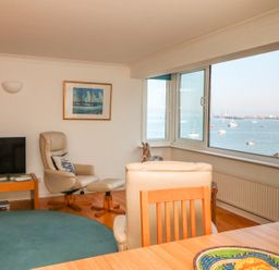 A living room with armchairs television and large windows overlooking a sea view at Port View in Falmouth