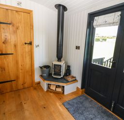 A corner of a room with a wood burning stove a wooden door and black double doors with glass panels at Cwt Y Rhos in Valley