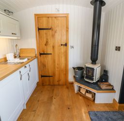 A kitchen corner with a wooden door a wood stove and white cabinets with a sink at Cwt Y Rhos in Valley