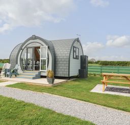 A small modern pod with outdoor chairs and a picnic table on a grassy area at Primrose in Seaton near Hornsea