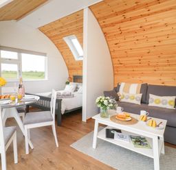 A small living area with a gray sofa and white coffee table next to a dining table and chairs with a bed in the background at Primrose in Seaton near Hornsea