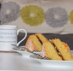 Two slices of sponge cake with jam on white plates and a white mug with blue text on a table at Primrose in Seaton near Hornsea