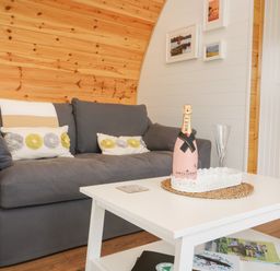 A grey sofa with cushions next to a white coffee table with a bottle and glass on it in a wooden room at Poppy Seaton near Hornsea