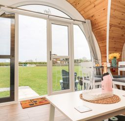 A dining area with a bottle of champagne on a table and large circular glass doors showing a grassy field at Poppy in Seaton near Hornsea