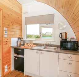 A small kitchen with wooden walls a sink a microwave a kettle a fridge and a window at Poppy in Seaton near Hornsea