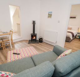 A living room with a wood-burning stove a dining table with chairs and a view into a bedroom at Ty Capel Bach in Rachub