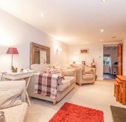 A living room with beige sofas a red rug a wooden mirror and lamp at Yanway Cottage in Troutbeck near Troutbeck Bridge