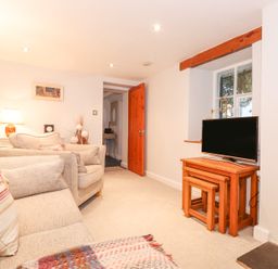 A living room with beige sofas a wooden tv stand with nested tables and a stone fireplace at Yanway Cottage in Troutbeck near Troutbeck Bridge