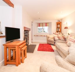 A living room with a television on wooden nesting tables a stone fireplace a red rug armchairs and a sofa with cushions at Yanway Cottage in Troutbeck near Troutbeck Bridge