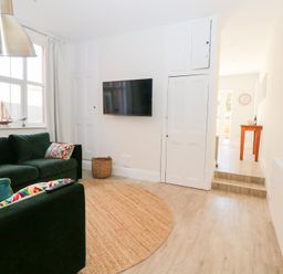 A living room with green sofas and colorful cushions a wall-mounted TV and a round rug at Flat 1 in Hunstanton