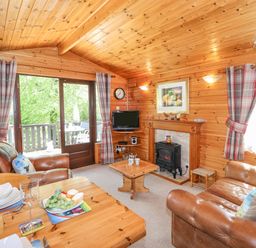 A wooden living room with leather sofas a small dining table set with plates a coffee table a fireplace with a stove and a television at Robins Nest Number 12 Burnside Park near Keswick