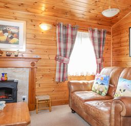 A wooden paneled living room with a brown leather sofa and a fireplace at Robins Nest Number 12 Burnside Park near Keswick