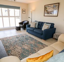 A living room with blue and beige sofas a patterned rug a black armchair a large window and a framed picture at Stillwaters in Bushmills County Antrim