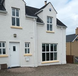 A white house with multiple windows a white door and gravel in front at Stillwaters in Bushmills County Antrim