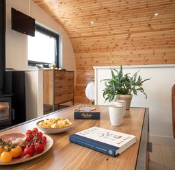 A living room with a wood stove a wooden table with snacks books and plants at Low Longlands in Cartmel