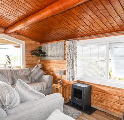 A living room with grey sofas a small stove and large windows at Ty Coed - 63 in Bronaber near Trawsfynydd
