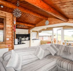 A living area with a striped gray sofa and kitchen cabinets in a wooden cabin at Ty Coed - 63 Bronaber near Trawsfynydd