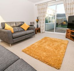 A living room with two grey sofas yellow cushions a yellow rug a wooden TV stand with a TV and sliding glass doors at Dunes View in Cubert