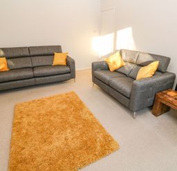 A living room with two gray sofas with yellow cushions a wooden side table with a lamp and an orange rug at Dunes View in Cubert