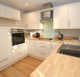 A kitchen with wooden countertops white cabinets built in oven microwave coffee machine electric stove and stainless steel sink at Dunes View in Cubert