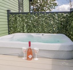 An outdoor hot tub with a bottle of prosecco and two white glasses on a wooden deck at Jeans Place in East Heslerton near West Heslerton