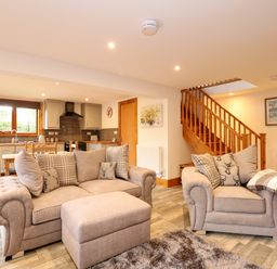 An open living room and kitchen area with beige sofas and wooden stairs at Little Lodge in Pentney near Kings Lynn